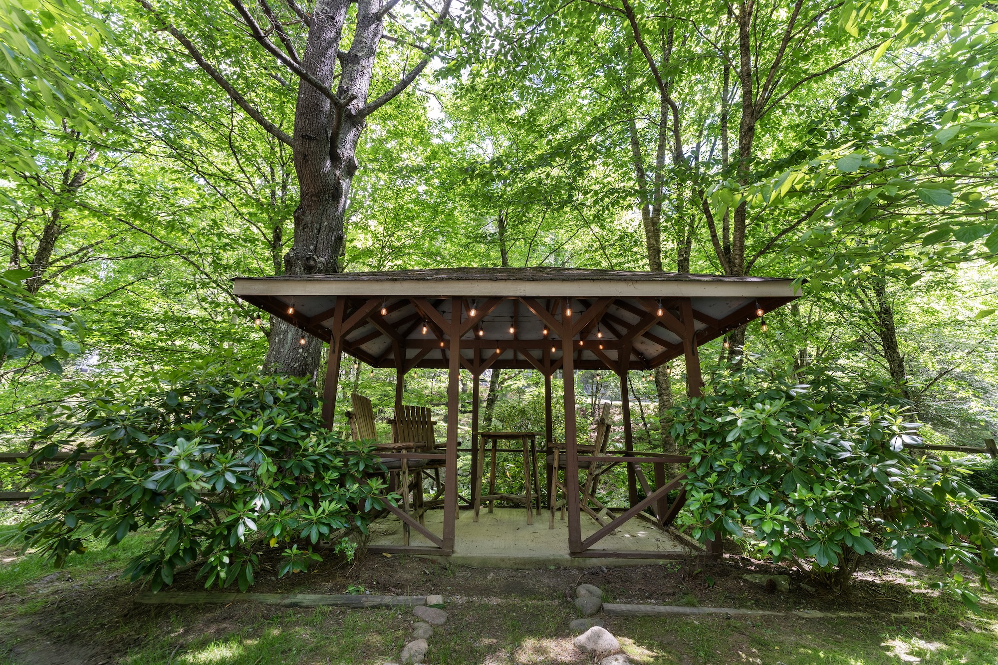 Gazebo with string lights surrounded by rhododendrons and mature trees